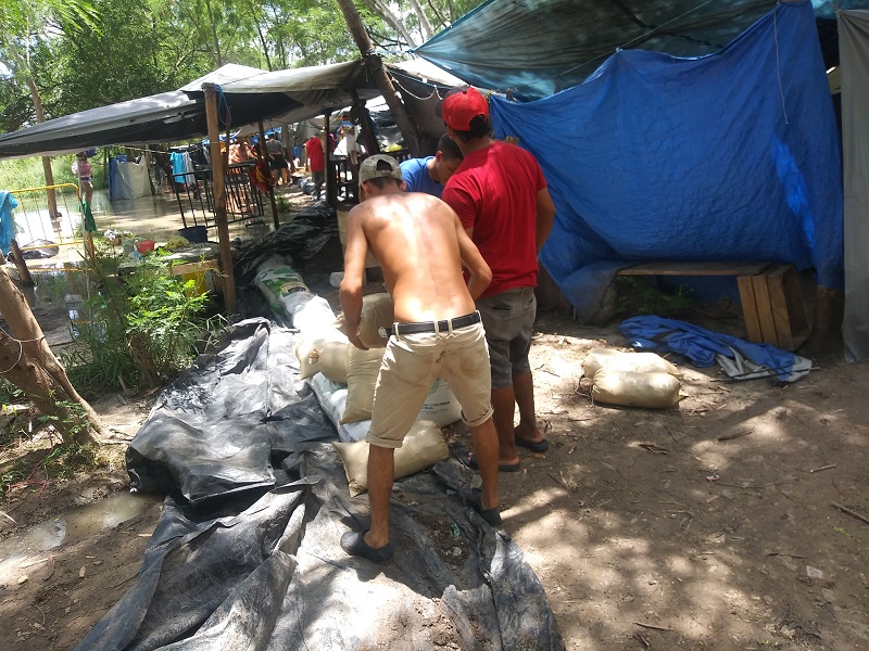 Migrantes intentan frenar creciente del río con costales de arena